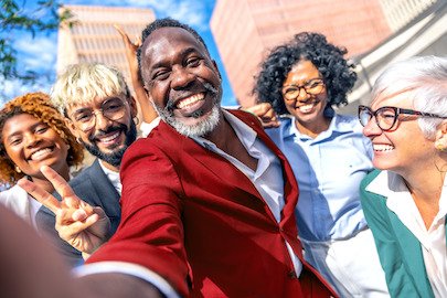 Människor i olika åldrar, av olika etnicitet och kön ler utanför en byggnad