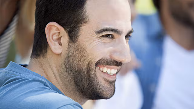 Profilbild på en ung man med skägg som ler och visar frisk munhälsa